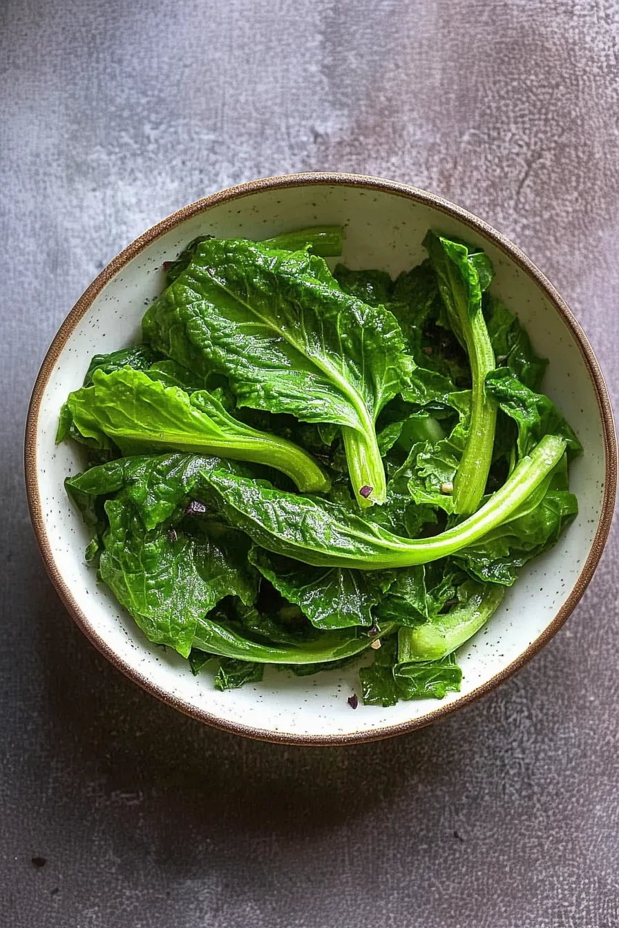 Shiny, wilted greens with visible stems and a sprinkle of pepper on top.