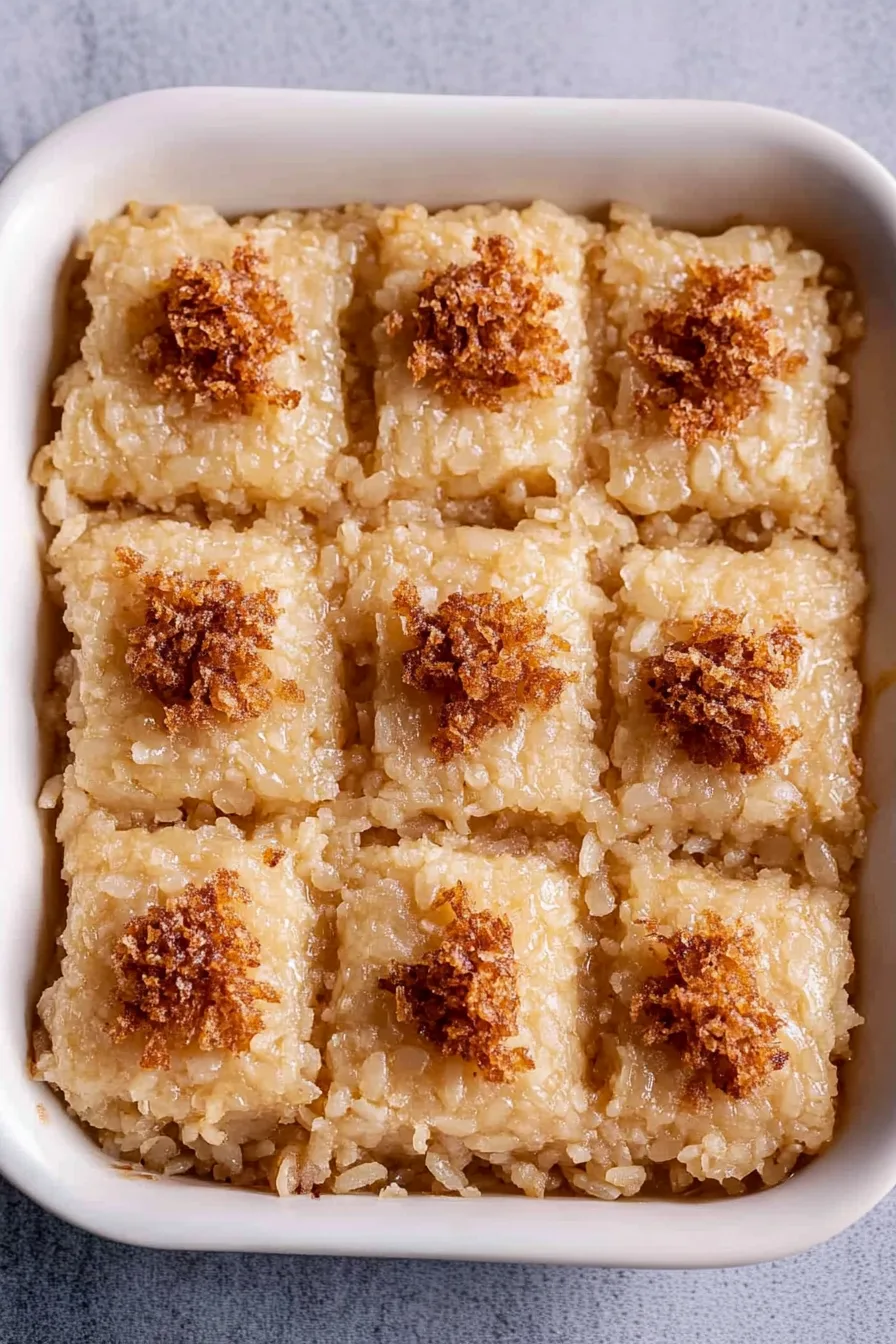 Sweet coconut rice squares arranged in rows with small mounds of toasted latik in the center.