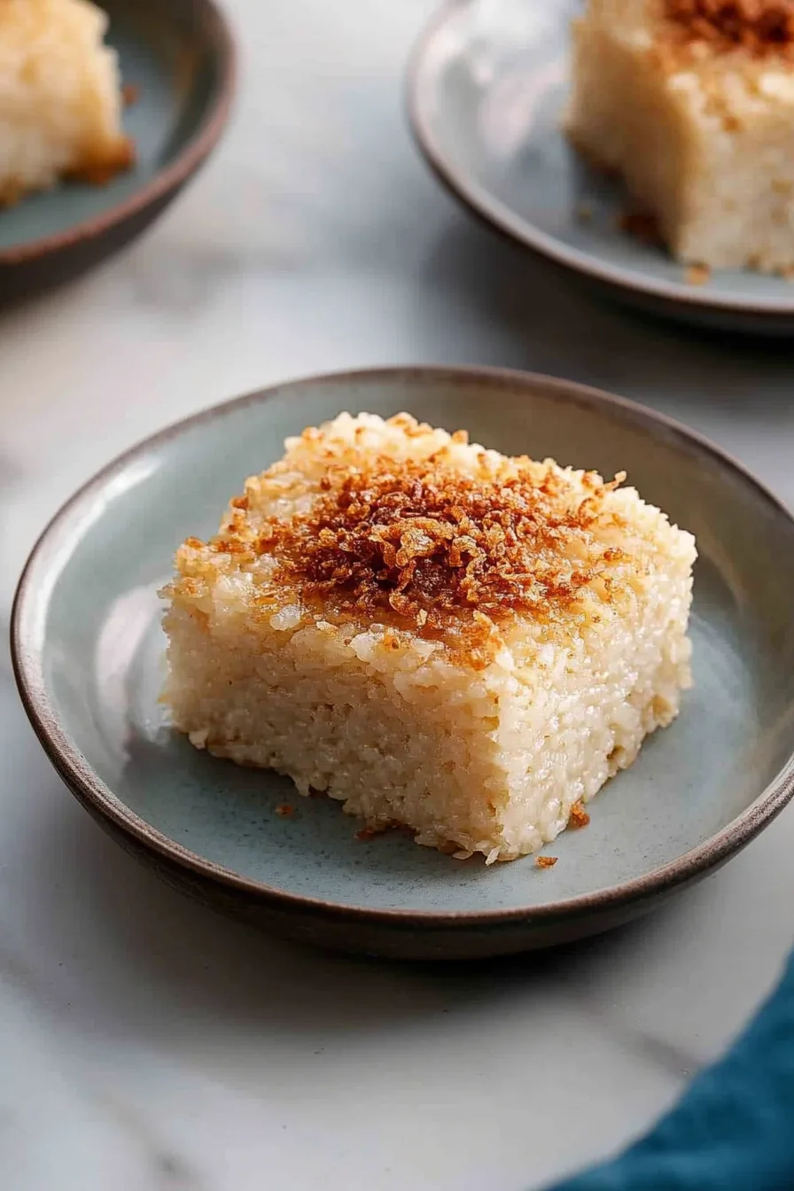 A plate of sticky coconut rice squares topped with golden latik, ready to serve.