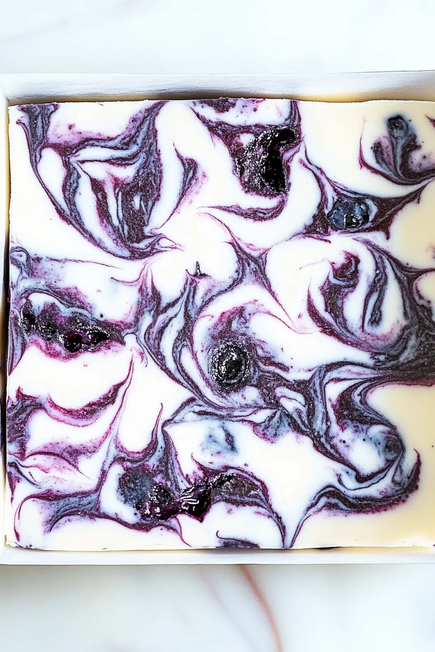 Smooth vanilla fudge with vibrant blueberry swirls and whole berries on top.