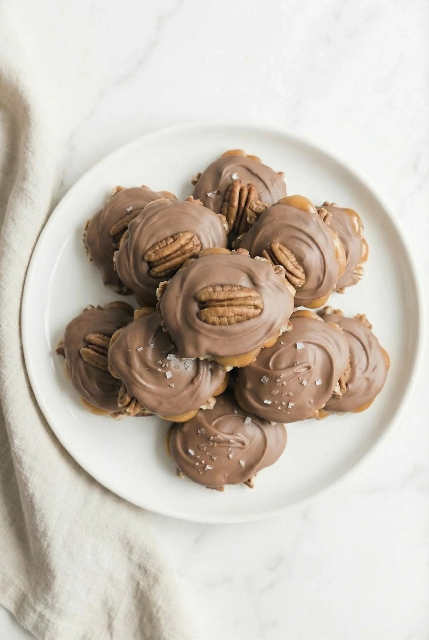 Overhead view of nutty caramel bites coated in soft chocolate, arranged neatly on a white dish.
