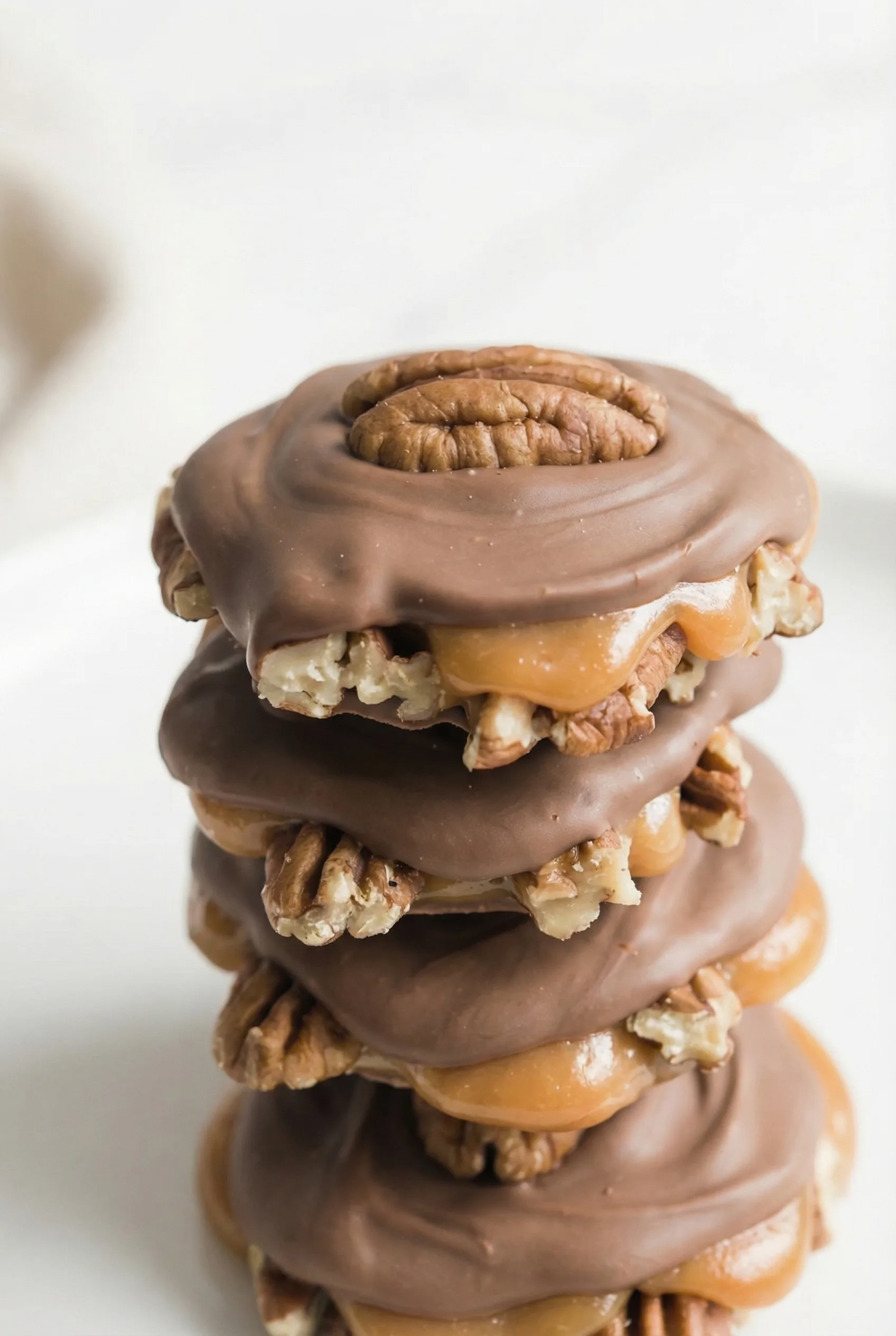 Close-up of caramel-pecan clusters topped with smooth milk chocolate on a marble surface.