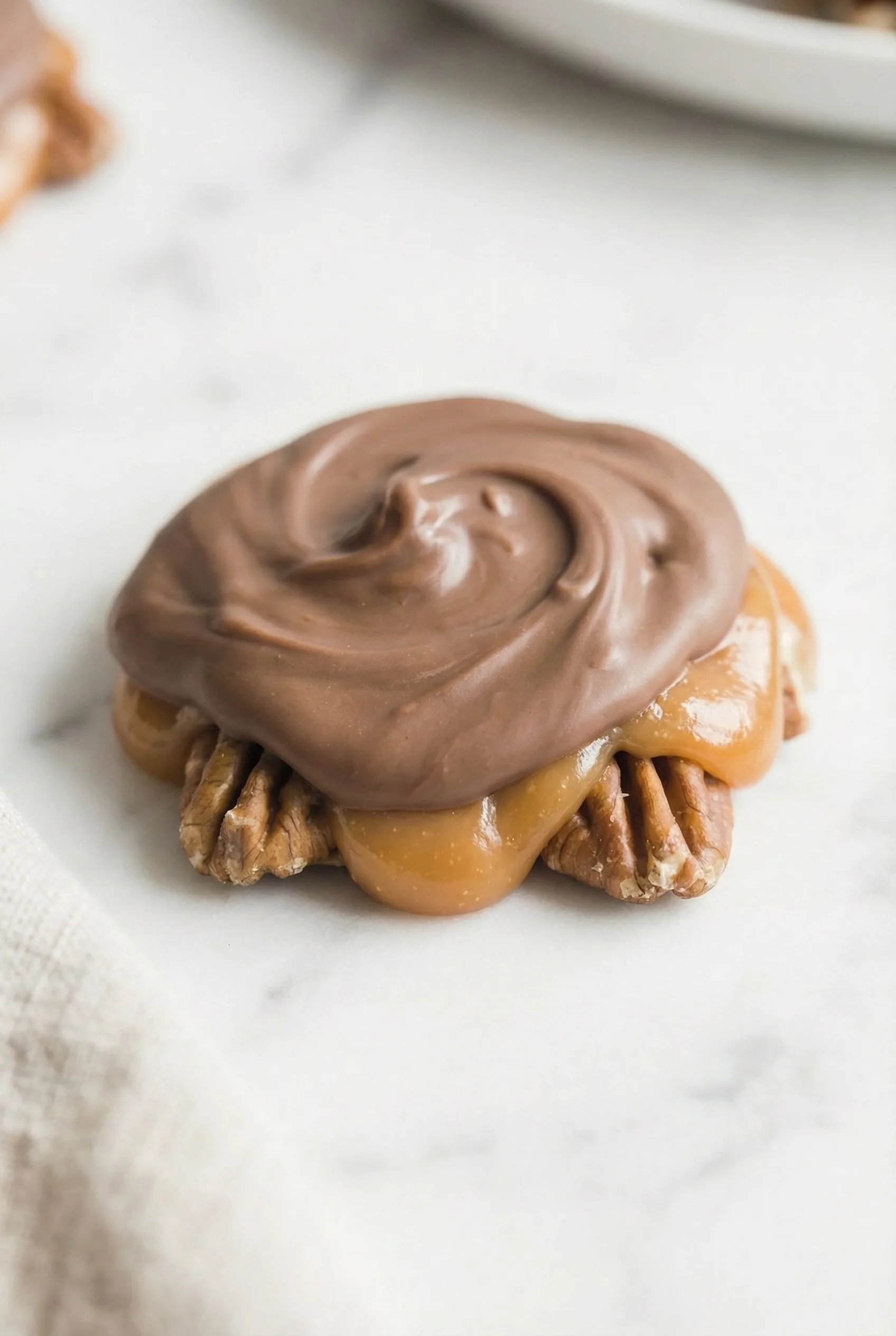 A rich, bite-sized candy with layered chocolate, caramel, and pecans, styled for a holiday dessert spread.