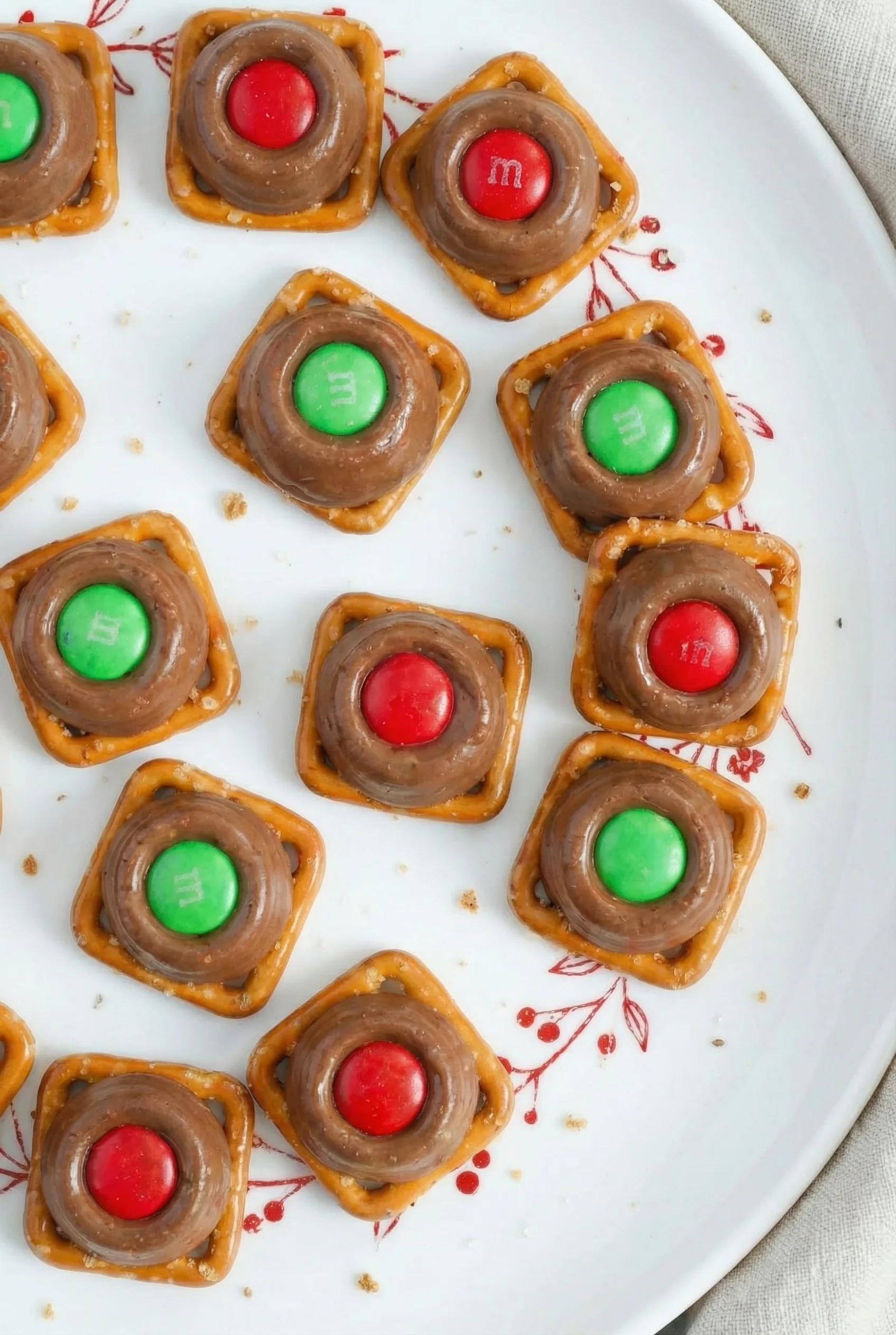 Several sweet-and-salty snacks arranged on a plate, each made with a square pretzel, a chocolate caramel candy, and an M&M.