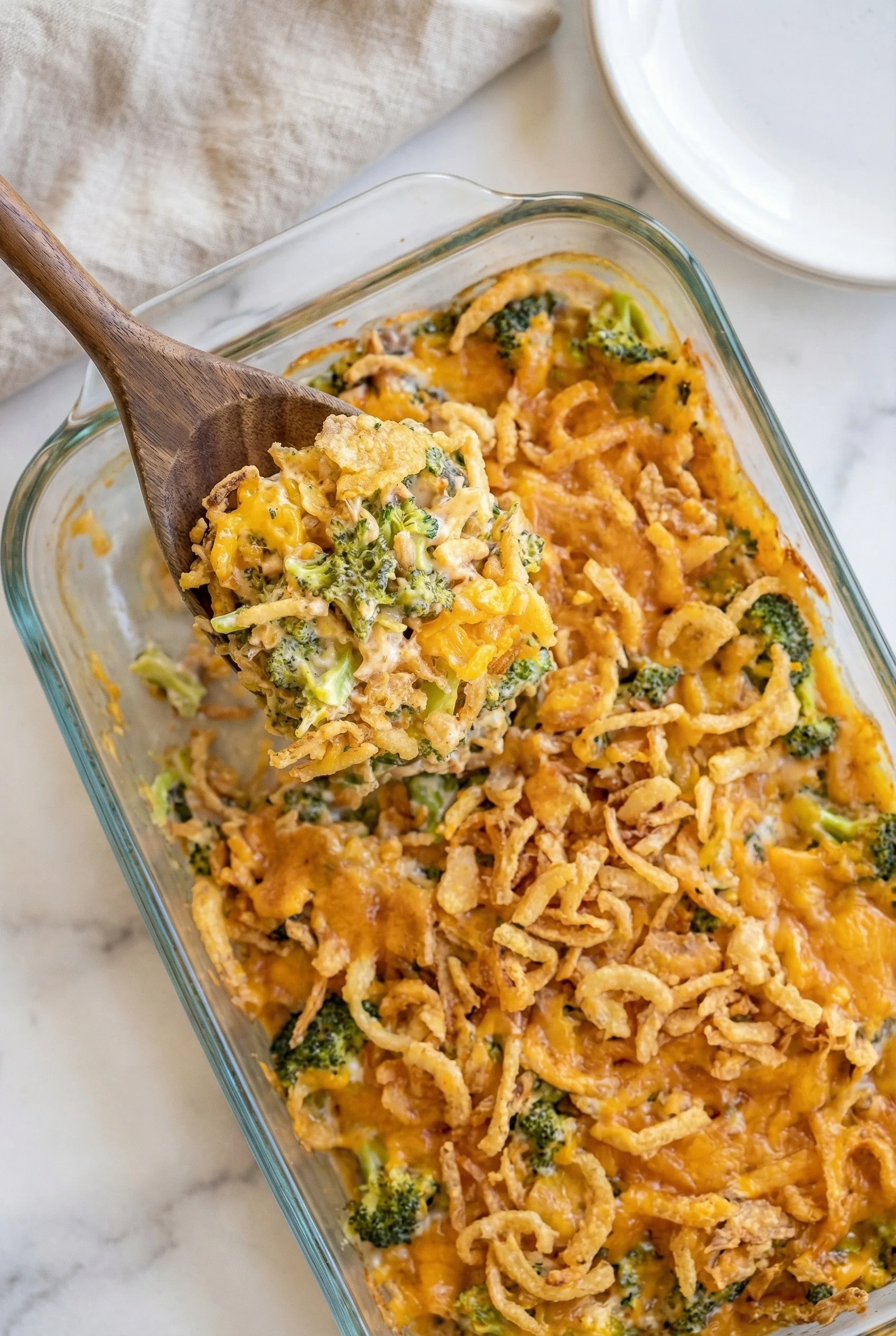 Spoonful lifted from a gooey, cheese-covered broccoli bake showing its creamy texture.