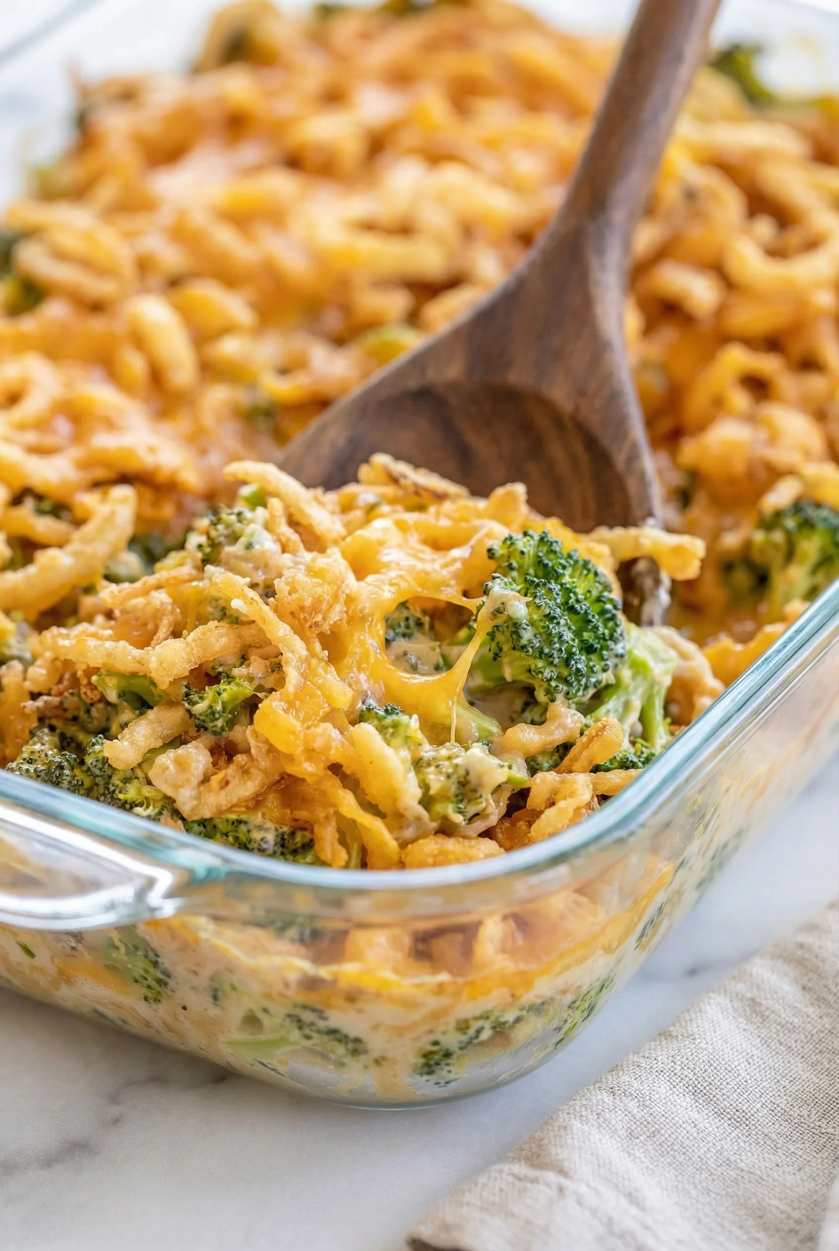 Spoon lifting a serving from a creamy, cheese-covered broccoli bake.