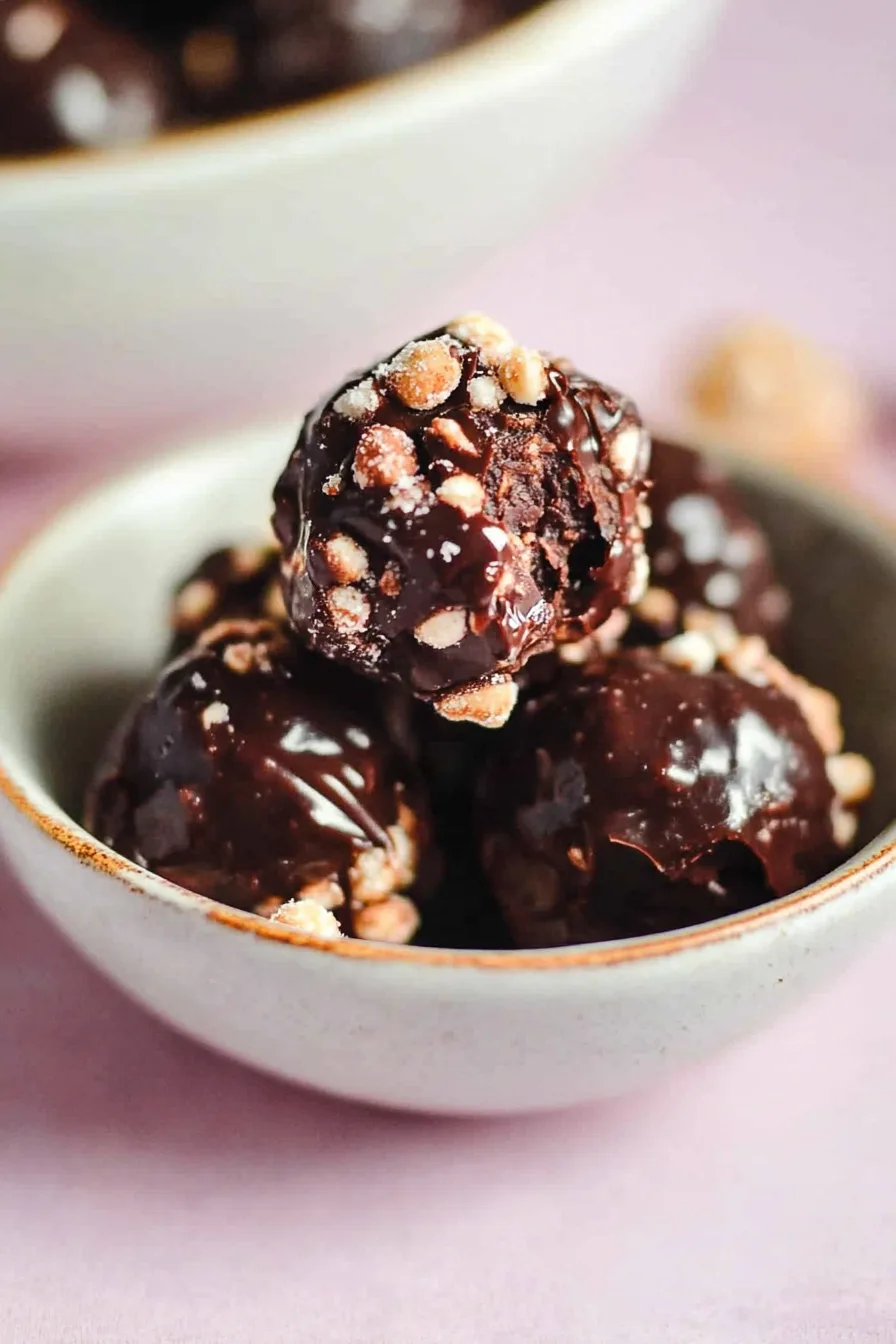 Stack of glossy, dark chocolate-coated treats with crunchy bits on the surface, arranged on a rustic plate.