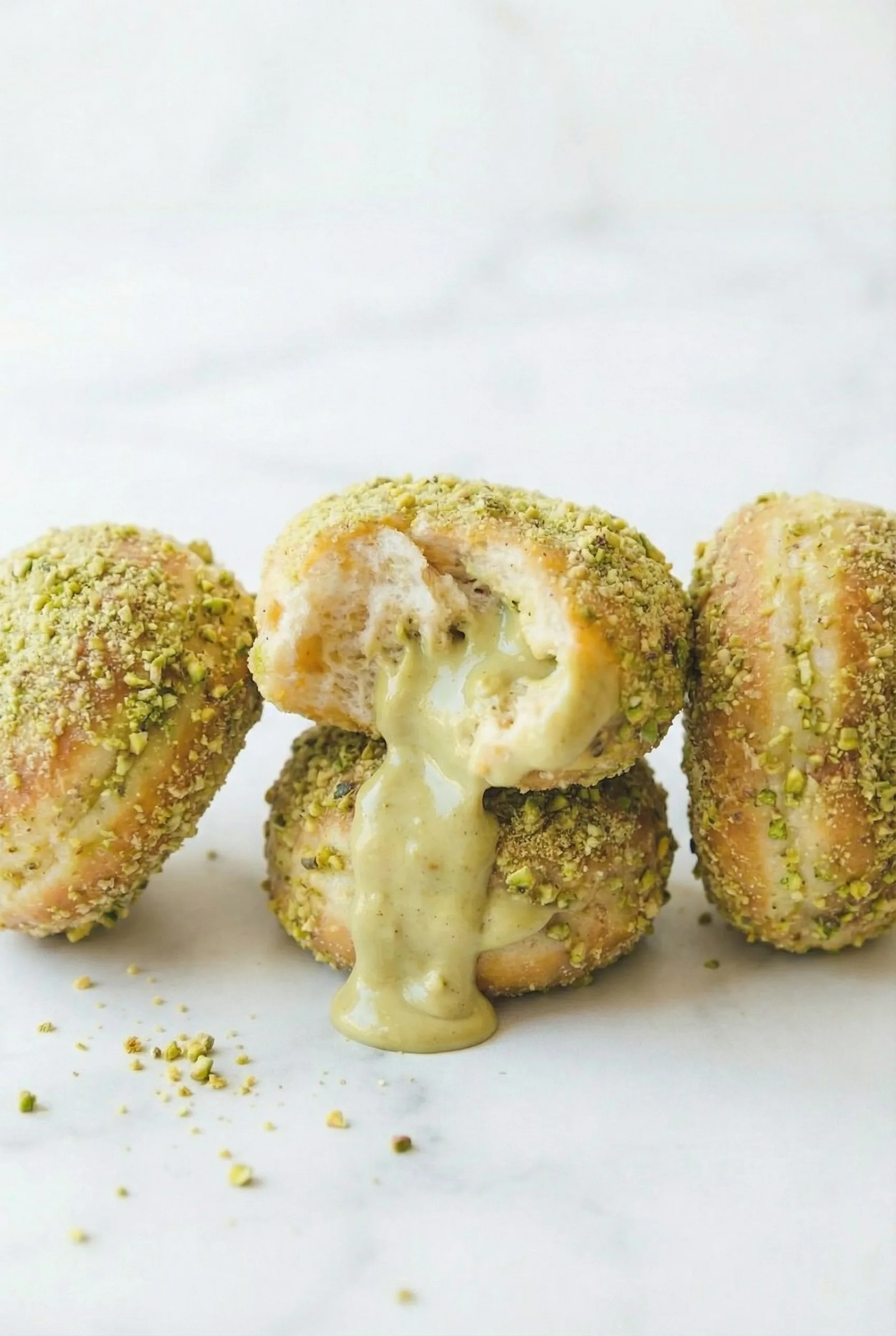A bitten donut resting on top of a stack, showing its smooth pistachio cream spilling onto the marble surface.