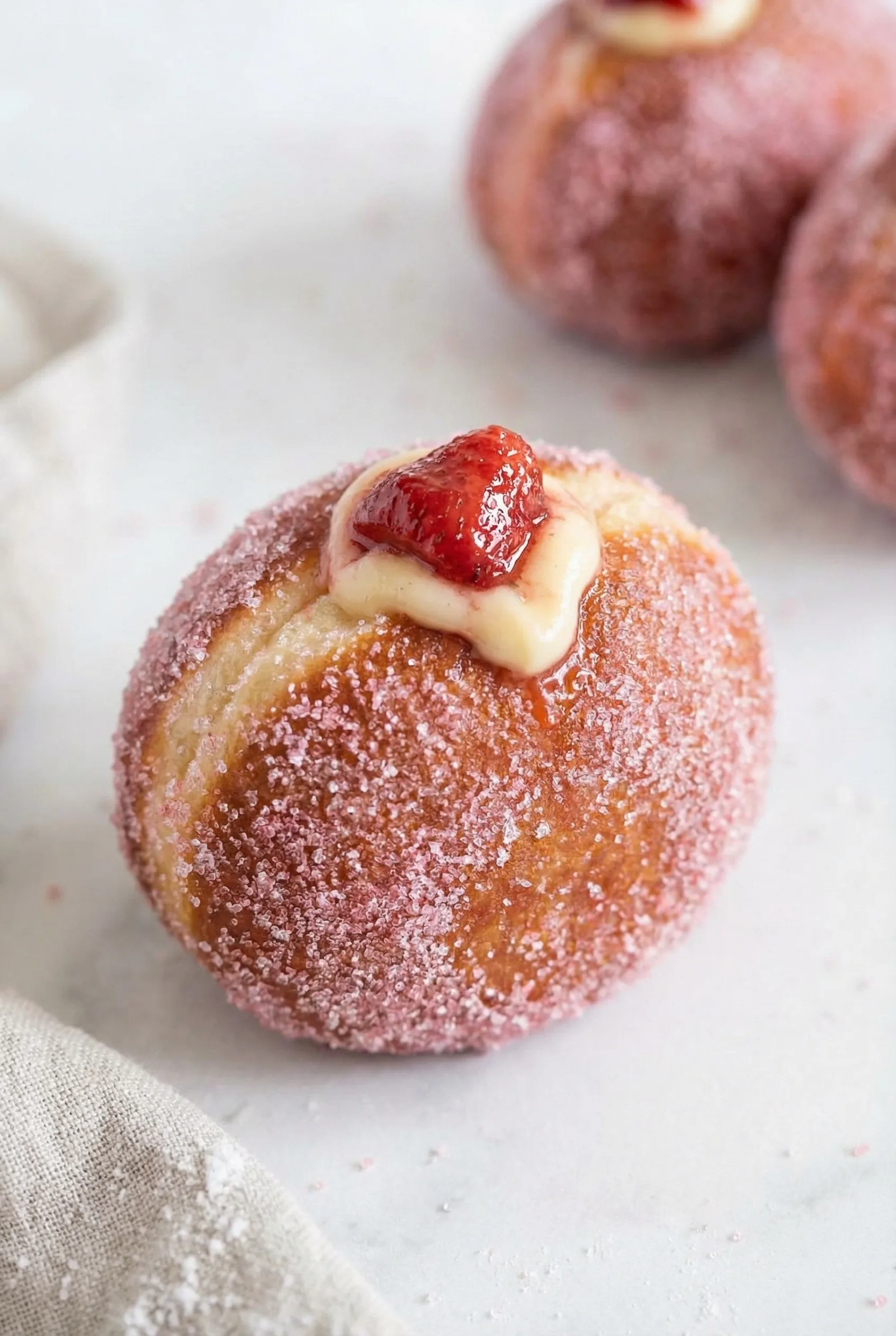 Close-up of a sugar-dusted doughnut with cream filling and a fresh strawberry on top.