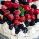 Close-up of a light, airy dessert piled with strawberries, blueberries, and raspberries.