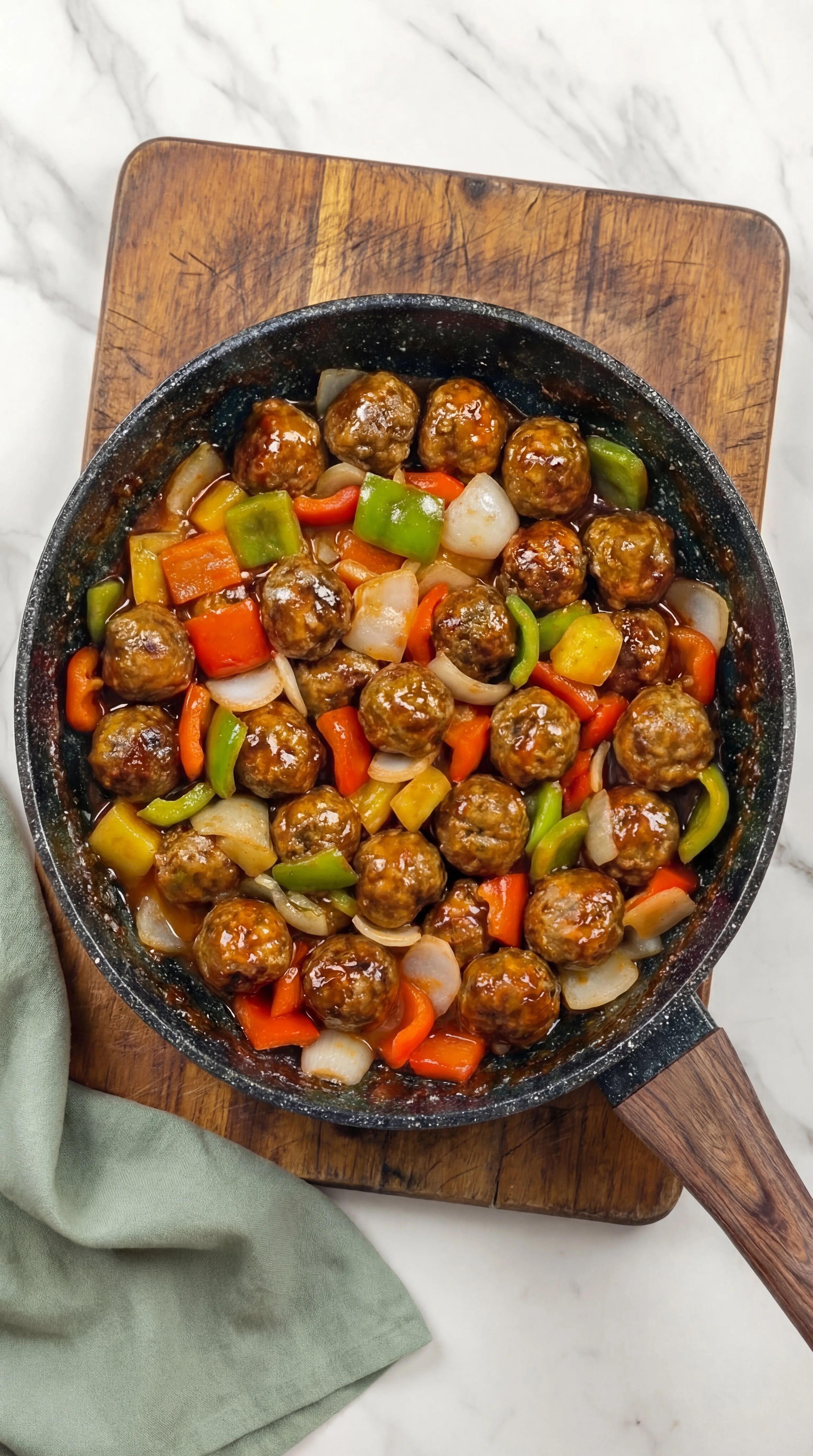 Sweet and Sour Meatballs cooked in skillet with bell peppers and onions in glossy sauce