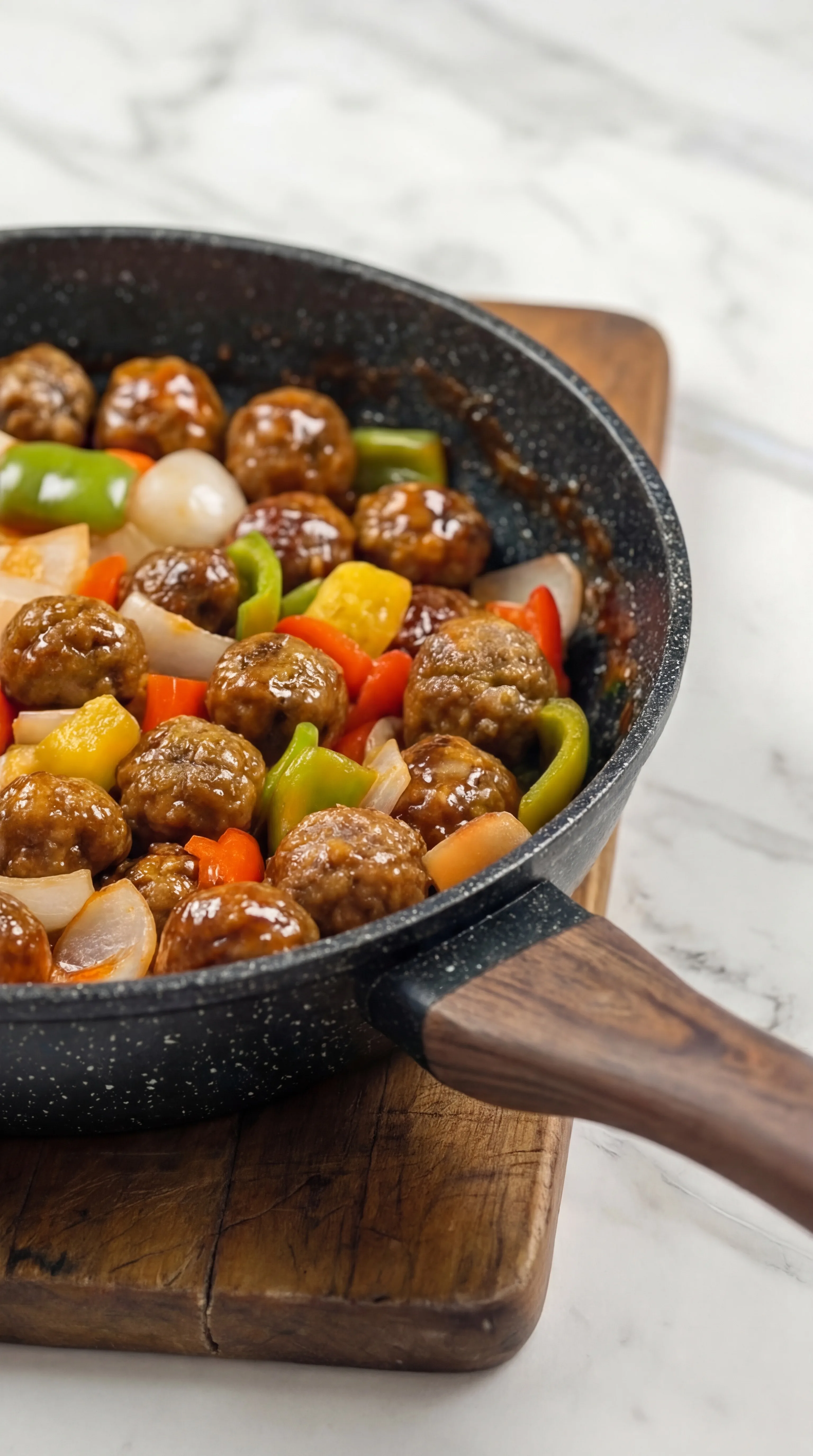 meatballs with red green and yellow peppers simmering in sweet tangy sauce in pan