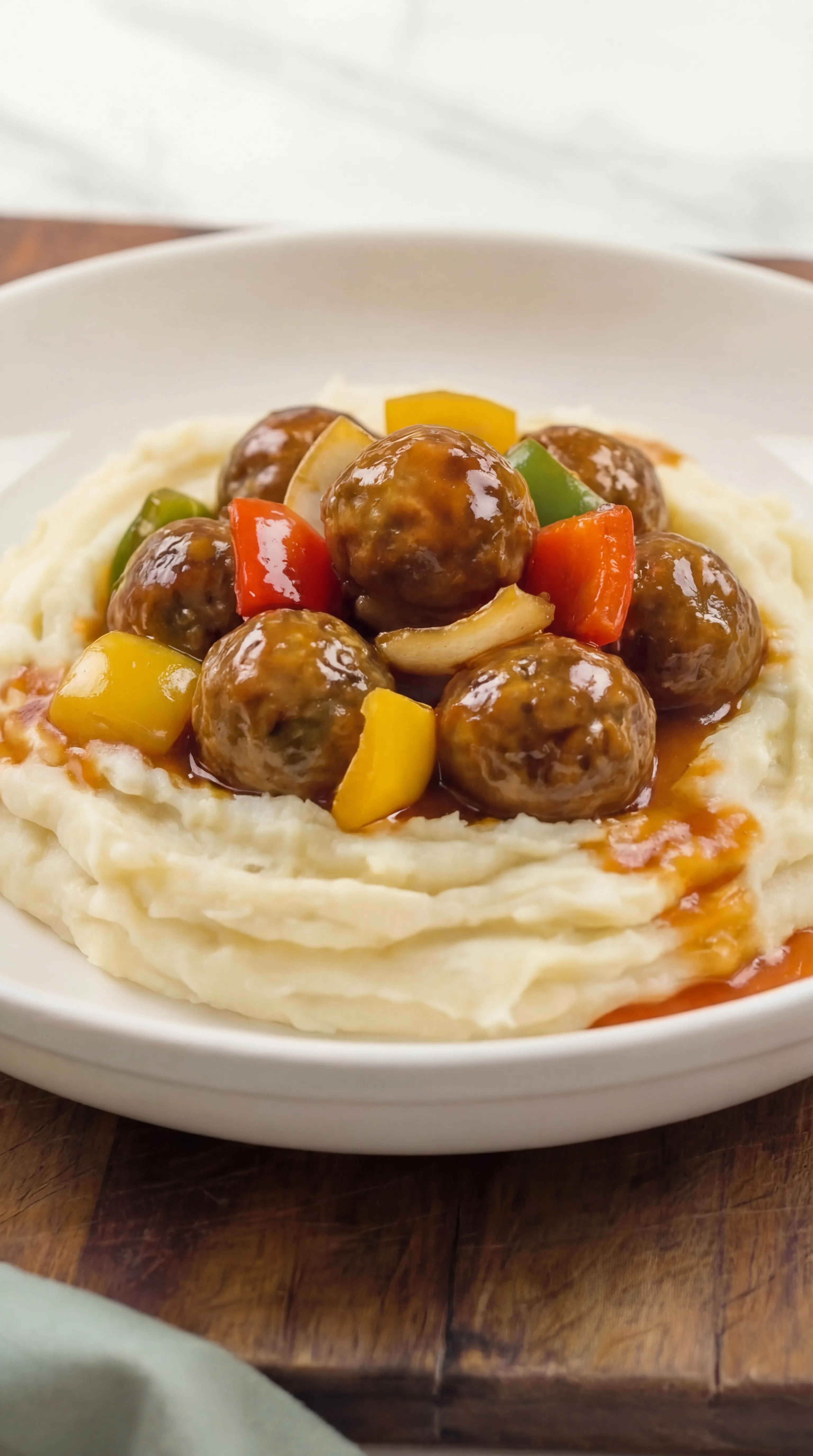 Sweet and Sour Meatballs plated on mashed potatoes with bell peppers and onions
