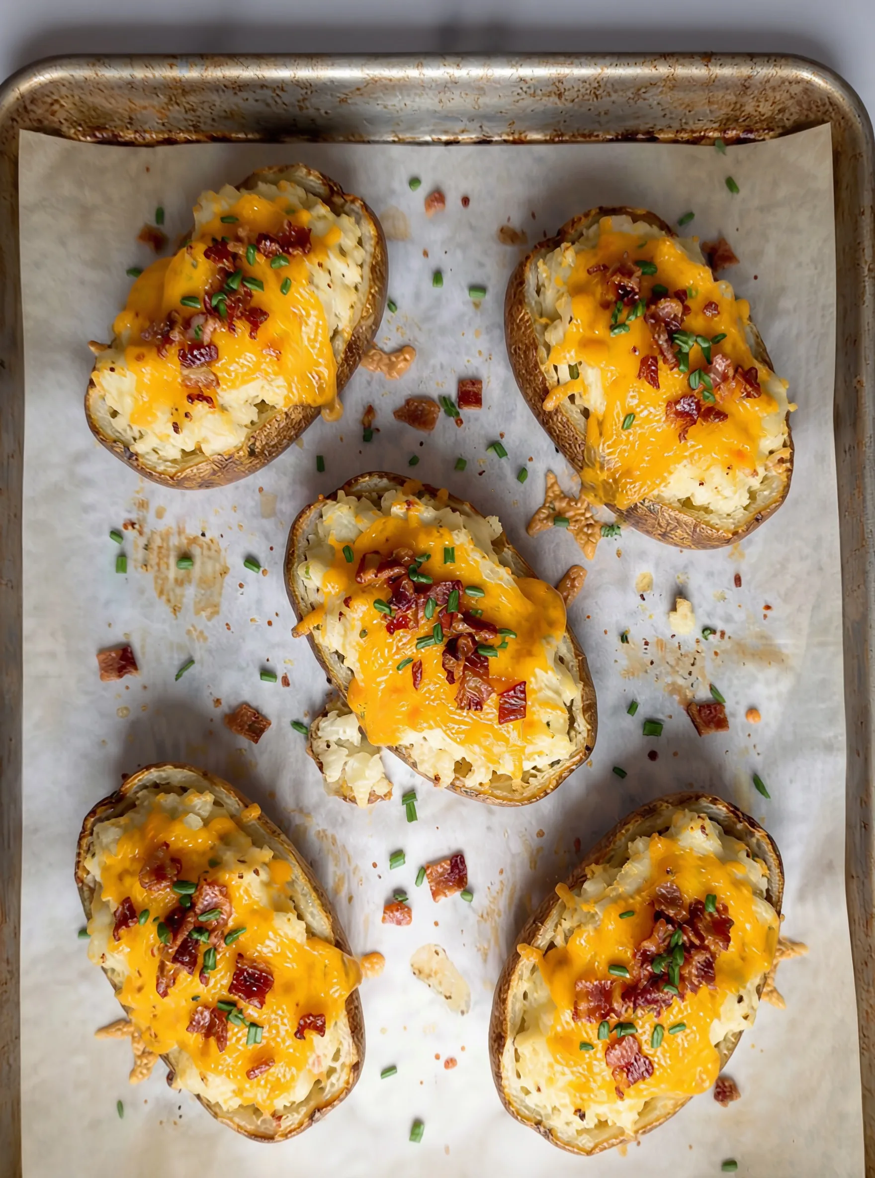 Twice Baked Potatoes filled with creamy mashed potatoes topped with melted cheddar cheese bacon and chives on baking sheet