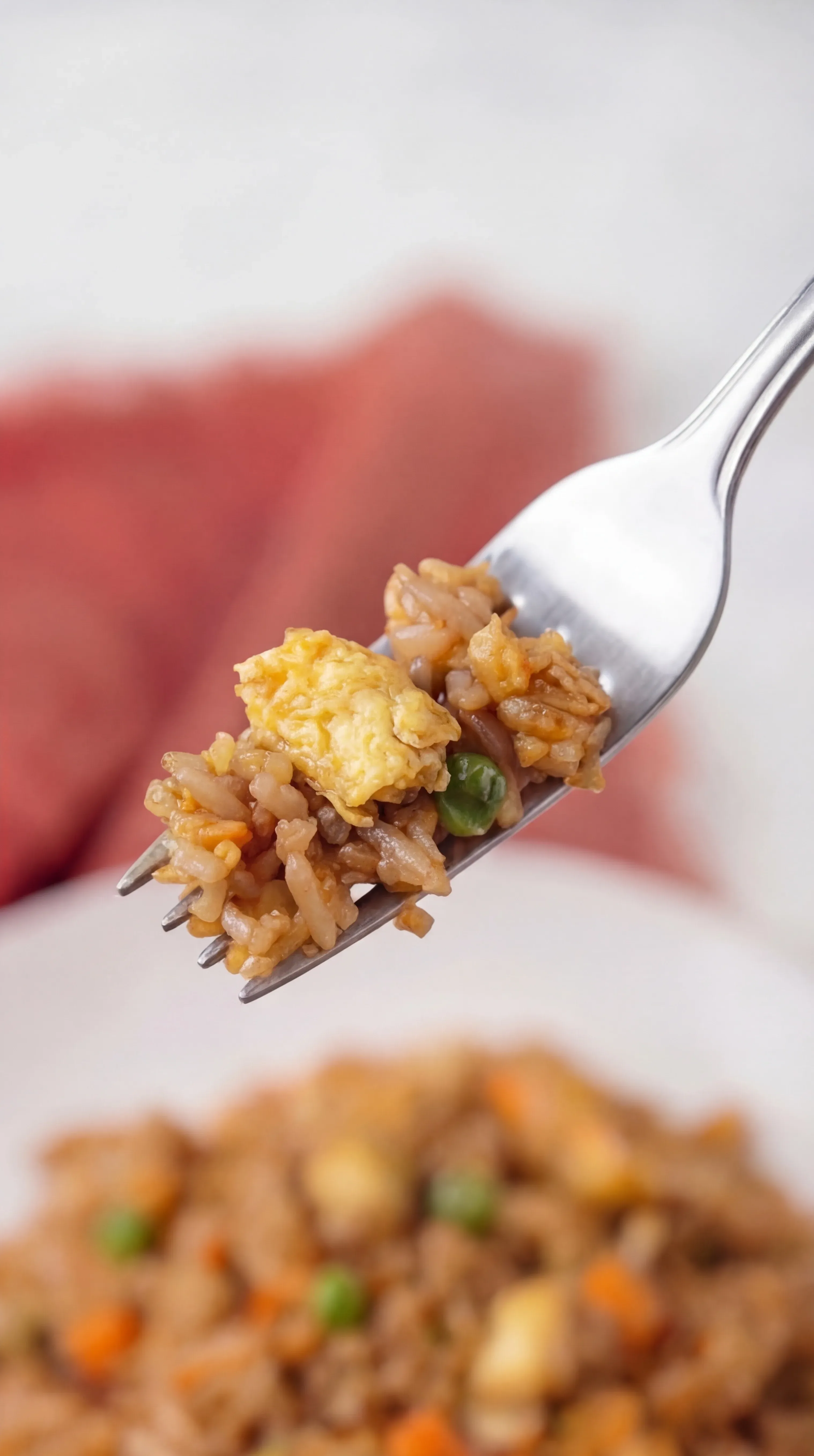 fork holding bite of fried rice with chicken egg peas and carrots