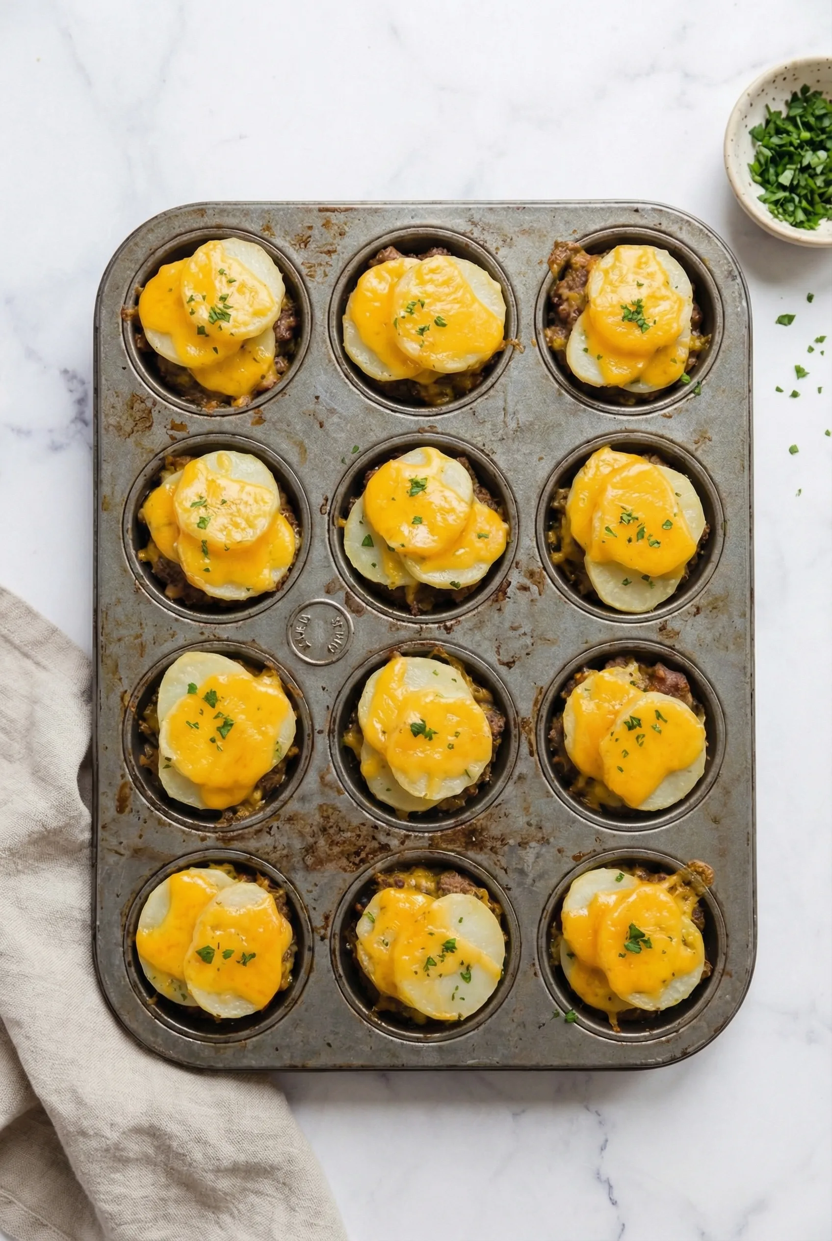 Meatloaf and Potatoes Recipe baked in muffin tin topped with sliced potatoes melted cheese and herbs